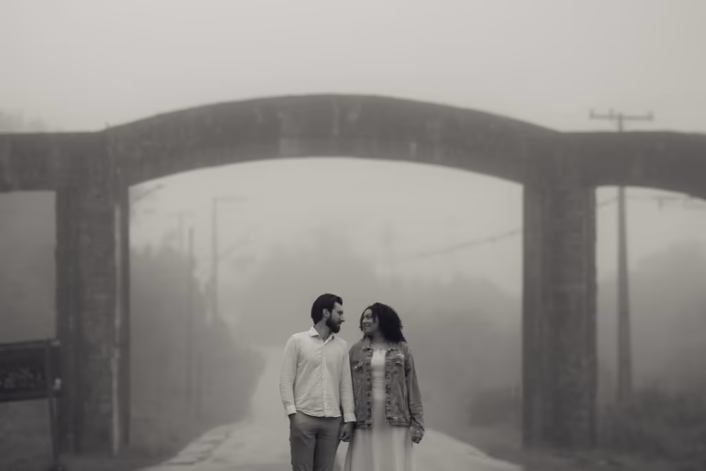 Casal caminhando numa estrada com neblina sob um arco