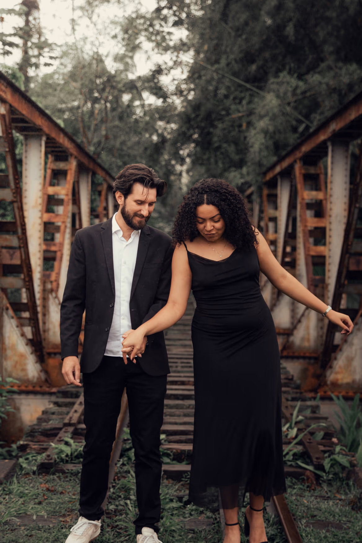 Casal de roupas pretas caminhando em uma ponte de ferro