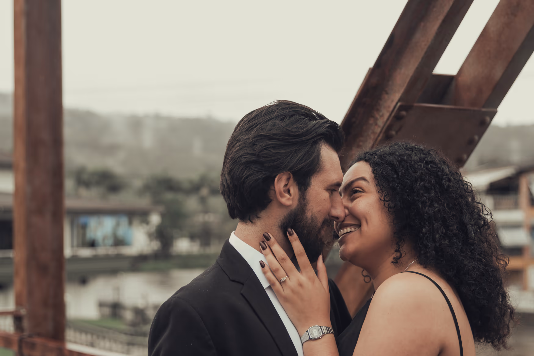 Casal quase se beijando em close com uma ponte ao fundo